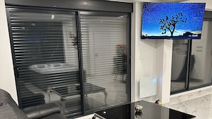 Een moderne woonkamer met een leren bank in het zwart, een glazen salontafel en een flatscreen televisie aan de wand bevestigd.