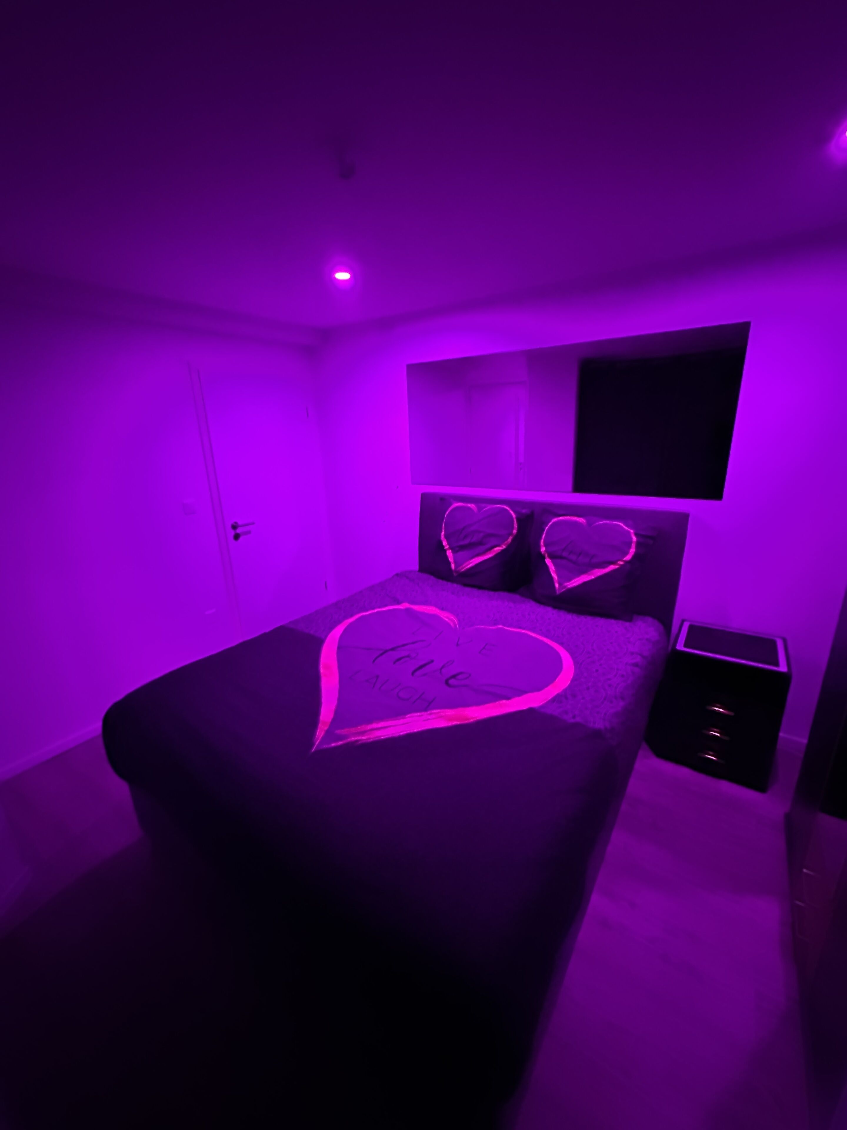 A bedroom with a bed, a nightstand, and a wall-mounted TV.