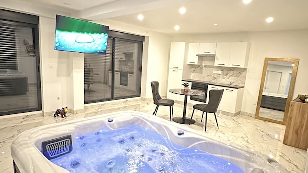 Een moderne badkamer met een ruime badkuip, een flatscreen televisie aan de muur en een klein tafeltje met stoelen.