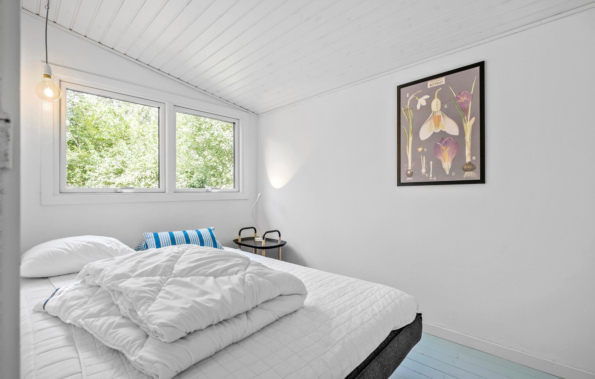A bedroom with a bed, a bedside table, a chair, and a window with a view of trees.
