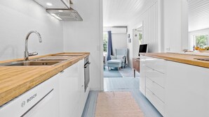 A modern kitchen with a Bosch dishwasher, wooden countertops, and a view into a living area with a blue chair and a TV. - Awesome home in Højby with WiFi (Højby)