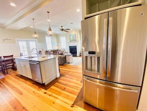 A spacious kitchen with a stainless steel refrigerator, wooden flooring, and pendant lighting.