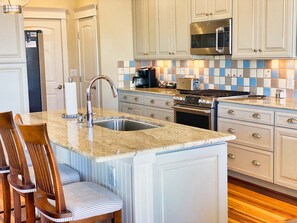 A kitchen with a granite countertop, stainless steel appliances, and a tiled backsplash. - Sunny Side Up - Chesapeake Properties (Cape Charles)