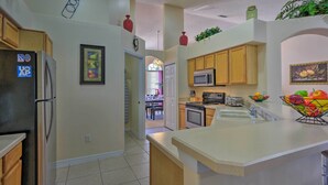 A kitchen with wooden cabinets, a refrigerator, a microwave, and a sink. There is a fruit bowl on the counter and a plant on the ceiling. - Cozy Nook Villa w/ Pool: 10 Mi to Park Entrance! (Clermont)