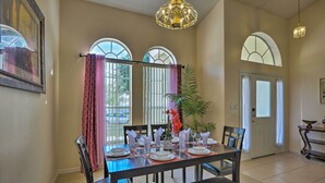 A dining area with a table set for four, large windows with curtains, a chandelier, and a door with a keypad lock. - Cozy Nook Villa w/ Pool: 10 Mi to Park Entrance! (Clermont)