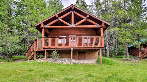 A two-story log cabin with a balcony, surrounded by a grassy yard and trees. - Trego Cabin w/ Mtn Views, Easy Access to Lake (Trego)