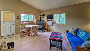 A cozy living room with a stone fireplace, a blue sofa, a wooden dining table, and a television mounted on the wall. - Trego Cabin w/ Mtn Views, Easy Access to Lake (Trego)