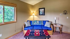 A room with a blue sofa, a small wooden table, a lamp, and a framed picture on the wall. - Trego Cabin w/ Mtn Views, Easy Access to Lake (Trego)