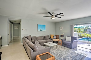 A living room with a sectional sofa, a coffee table, a side table, and a ceiling fan. There is a view of a swimming pool through large windows. - Cape Coral Waterfront Getaway w/ Kayaks & Bikes! (Cape Coral)