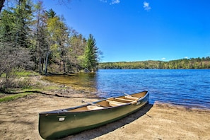 Un canoë sur une plage de sable, au bord d’un lac paisible, entouré d’arbres.