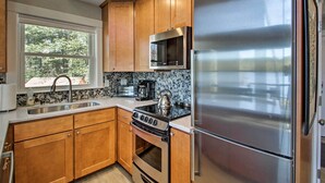 Una cocina con armarios de madera, un refrigerador de acero inoxidable, un microondas, una estufa y una ventana con vista a árboles.