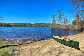 Un canoë sur une plage de sable, au bord d’un lac paisible, avec des arbres en arrière-plan.
