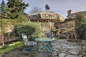 A patio with a glass table and chairs, an umbrella, and a stone fire pit. - Seattle Area Getaway ~ 5 Mi to Puget Sound! (Mountlake Terrace)
