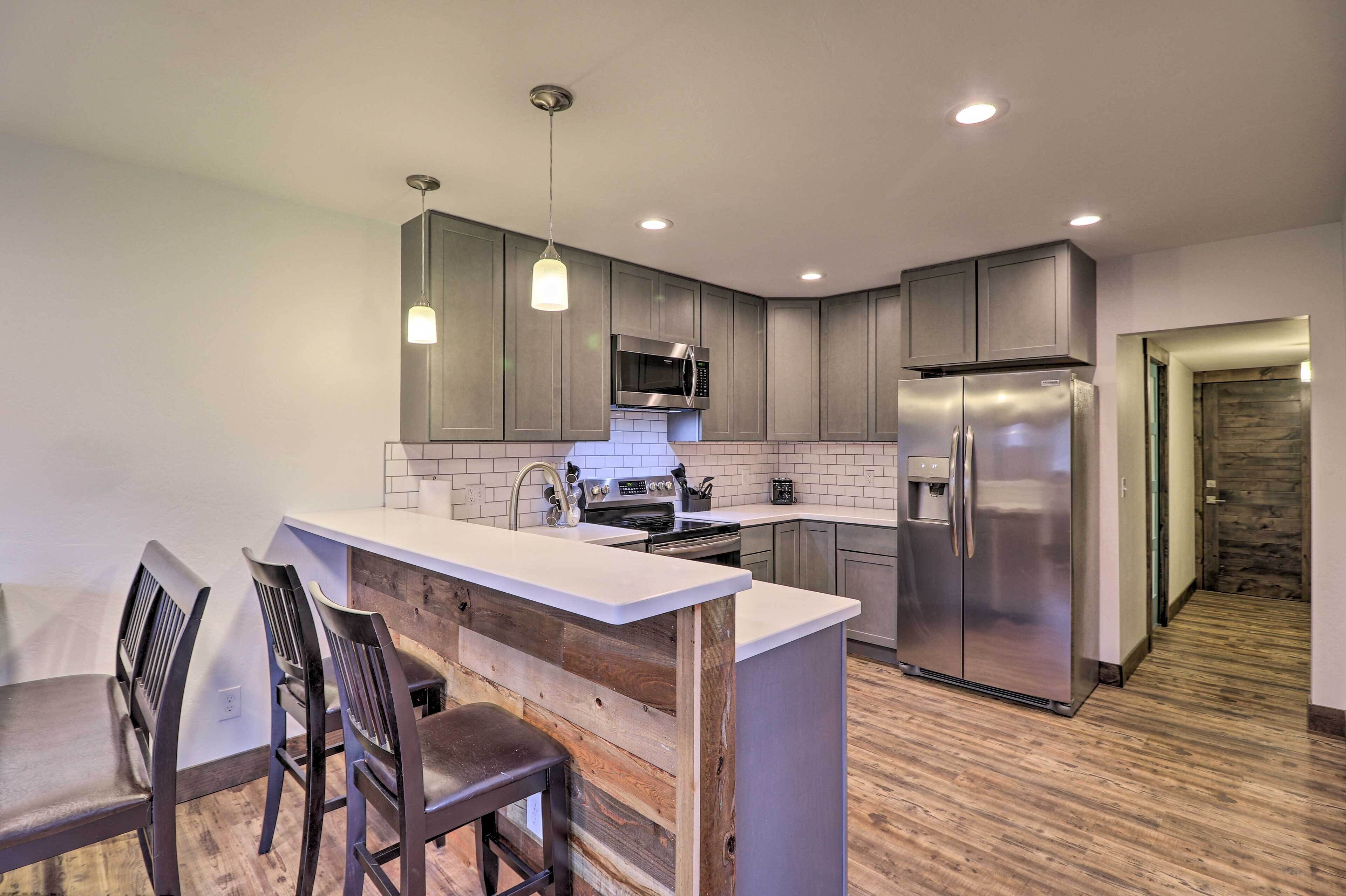 A modern kitchen with grey cabinets, stainless steel appliances, a wooden island, and a bar stool.