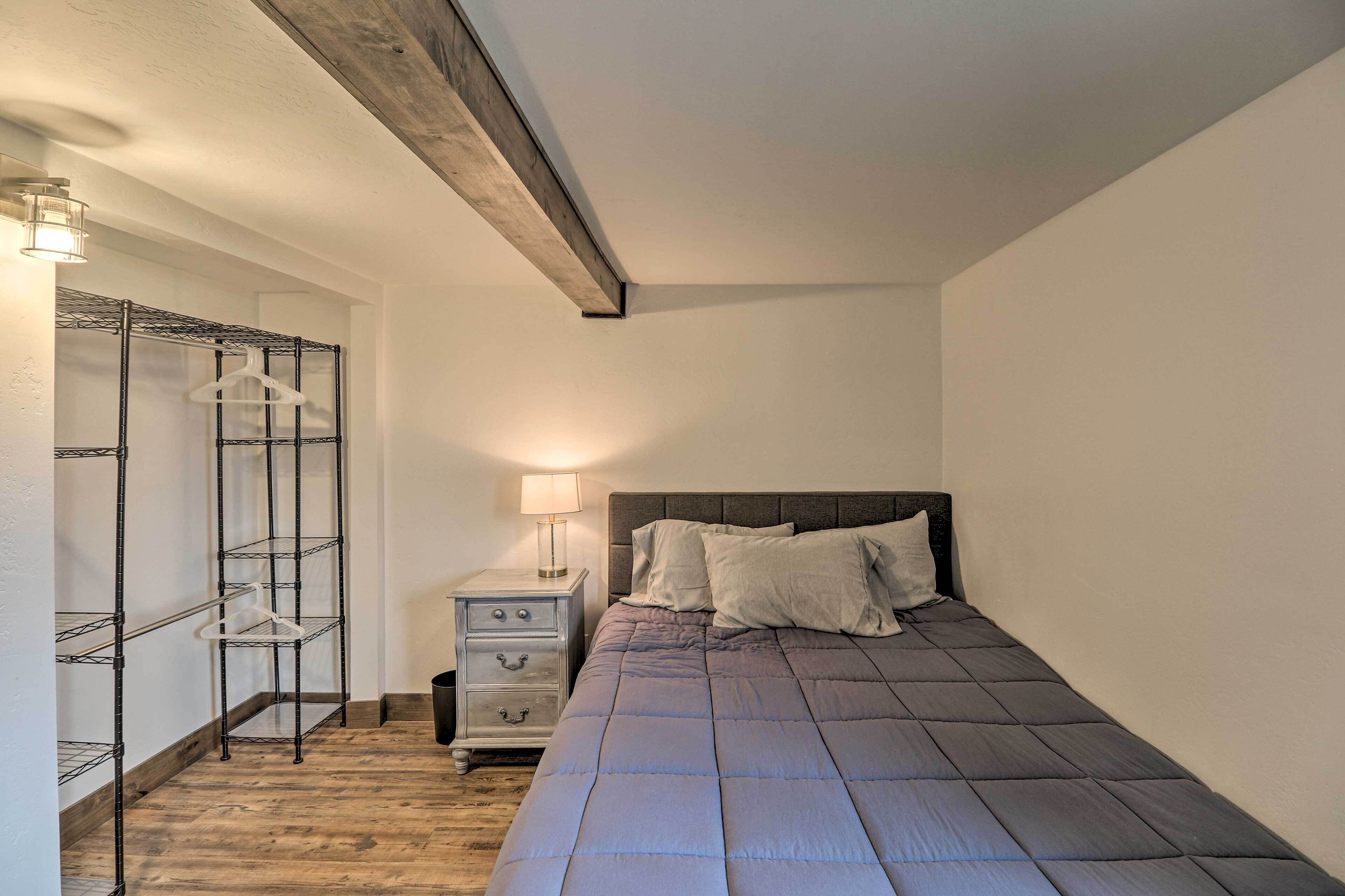 A bedroom with a bed, a nightstand, a lamp, and a metal shelving unit.