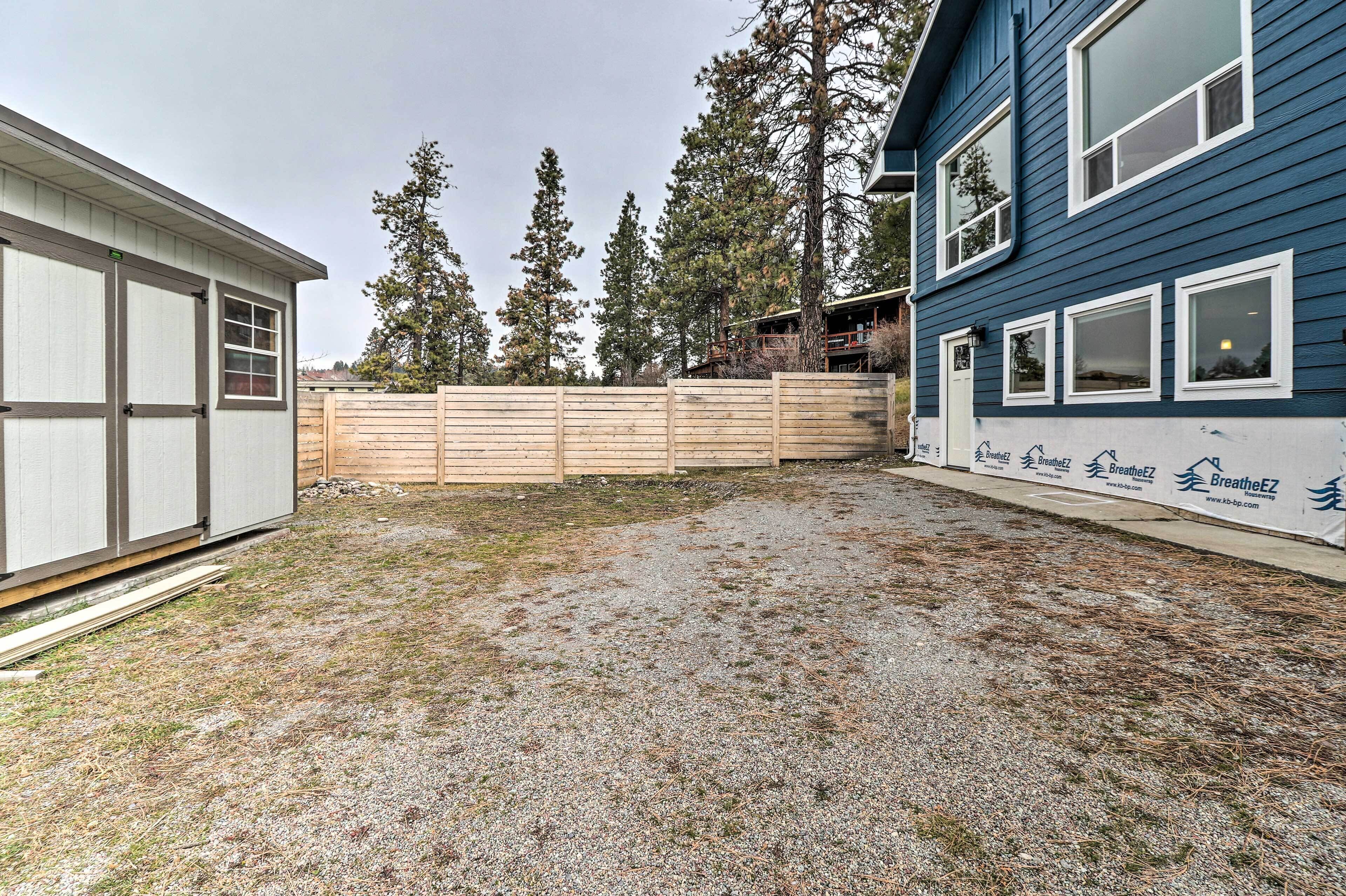 A backyard with a wooden fence, a gravel area, and a building with a blue exterior.