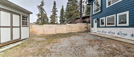 A backyard with a wooden fence, a gravel area, and a building with a blue exterior.