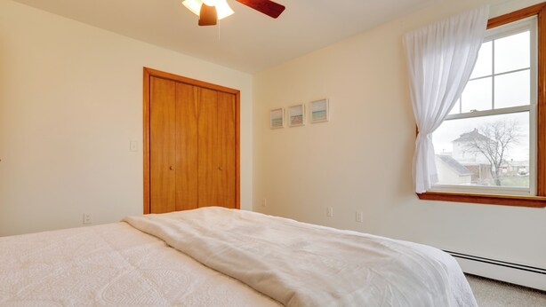 Un dormitorio con una cama grande, una puerta de madera, una ventana con cortinas y un ventilador de techo.