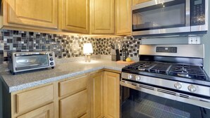 Una cocina con armarios de madera, un microondas de acero inoxidable, un tostador y una estufa a gas.