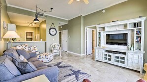 Un salon avec un canapé gris, un tapis orné de motifs en étoile, un meuble de télévision blanc et un ventilateur de plafond.