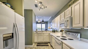 Une cuisine avec des armoires blanches, un réfrigérateur, une cuisinière et un four à micro-ondes. Il y a une fenêtre donnant sur l’extérieur.