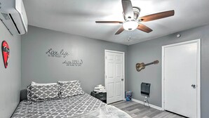 Une chambre à coucher avec un lit, un ventilateur de plafond, une guitare et une citation inspirante sur le mur.