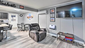Un salon moderne avec un fauteuil inclinable en cuir, un coin repas avec une table et des chaises, un téléviseur à écran plat fixé au mur et une petite étagère remplie de livres.