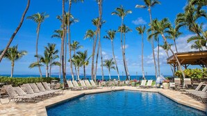 A poolside area with palm trees, lounge chairs, and a view of the ocean. - Mana Kai #614 2 Bedroom Condo (Kihei)