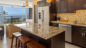 A modern kitchen with a large island, dark wood cabinets, and pendant lighting. - Mana Kai #614 2 Bedroom Condo (Kihei)