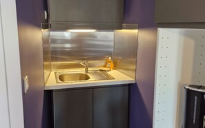 Cocina de acero inoxidable con un lavamanos, una botella de detergente y un cubo de basura.