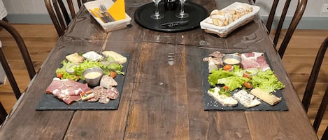 A wooden dining table with two black slate boards, each holding an assortment of cheeses, meats, and vegetables.