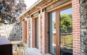 A building with a stone wall, a glass door, and a small outdoor seating area with metal chairs.