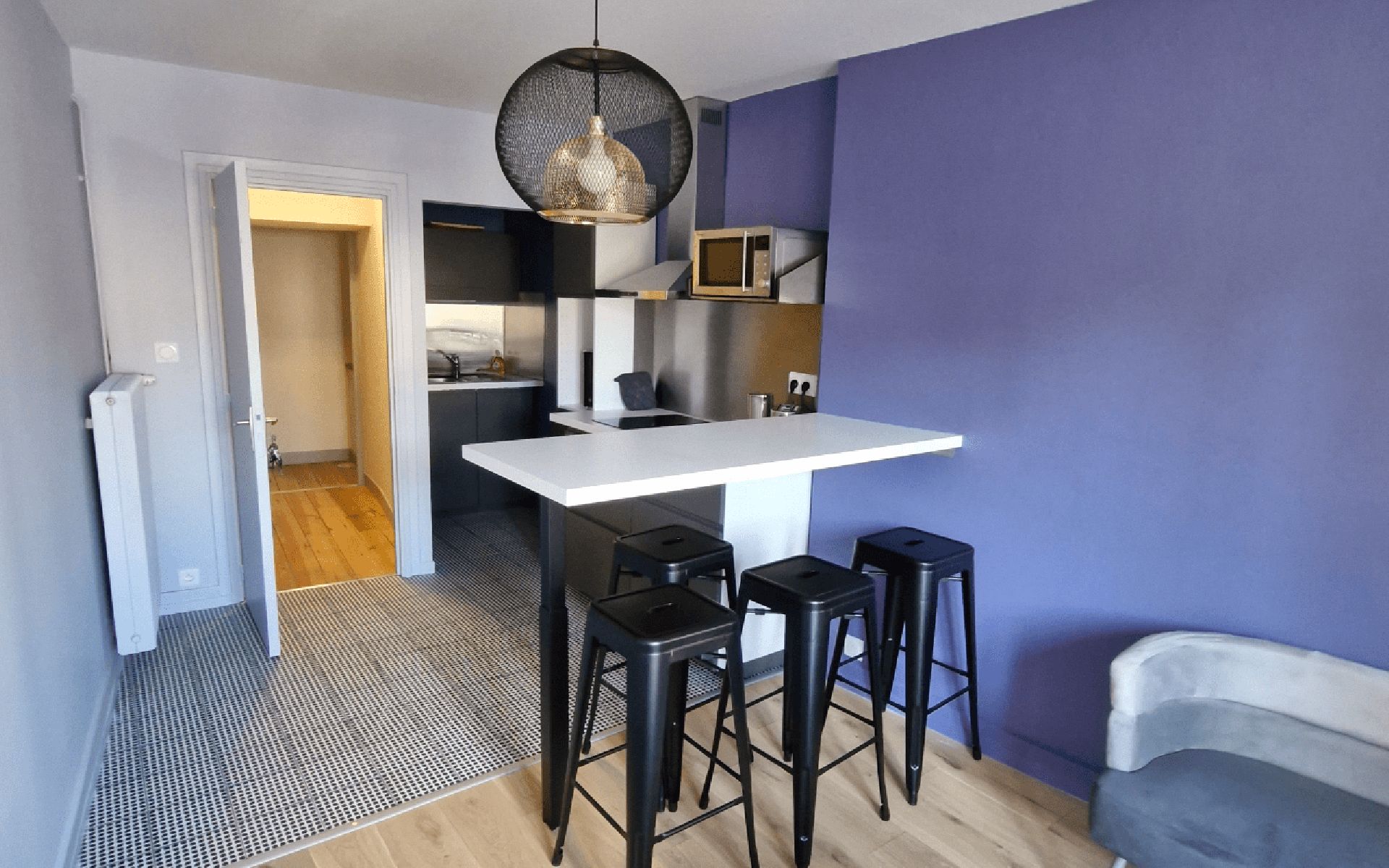 A compact kitchen with a white countertop, black stools, and a hanging light fixture.