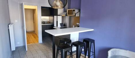 A compact kitchen with a white countertop, black stools, and a hanging light fixture.