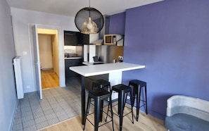 A compact kitchen with a white countertop, black stools, and a hanging light fixture.
