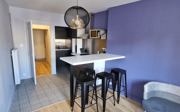 A compact kitchen with a white countertop, black stools, and a hanging light fixture.