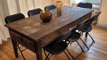 Una mesa de comedor de madera con sillas, un florero y una ventana al fondo.