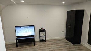 Une chambre dotée d’un téléviseur à écran plat posé sur un meuble, d’une petite étagère avec des articles de toilette et d’une armoire noire.