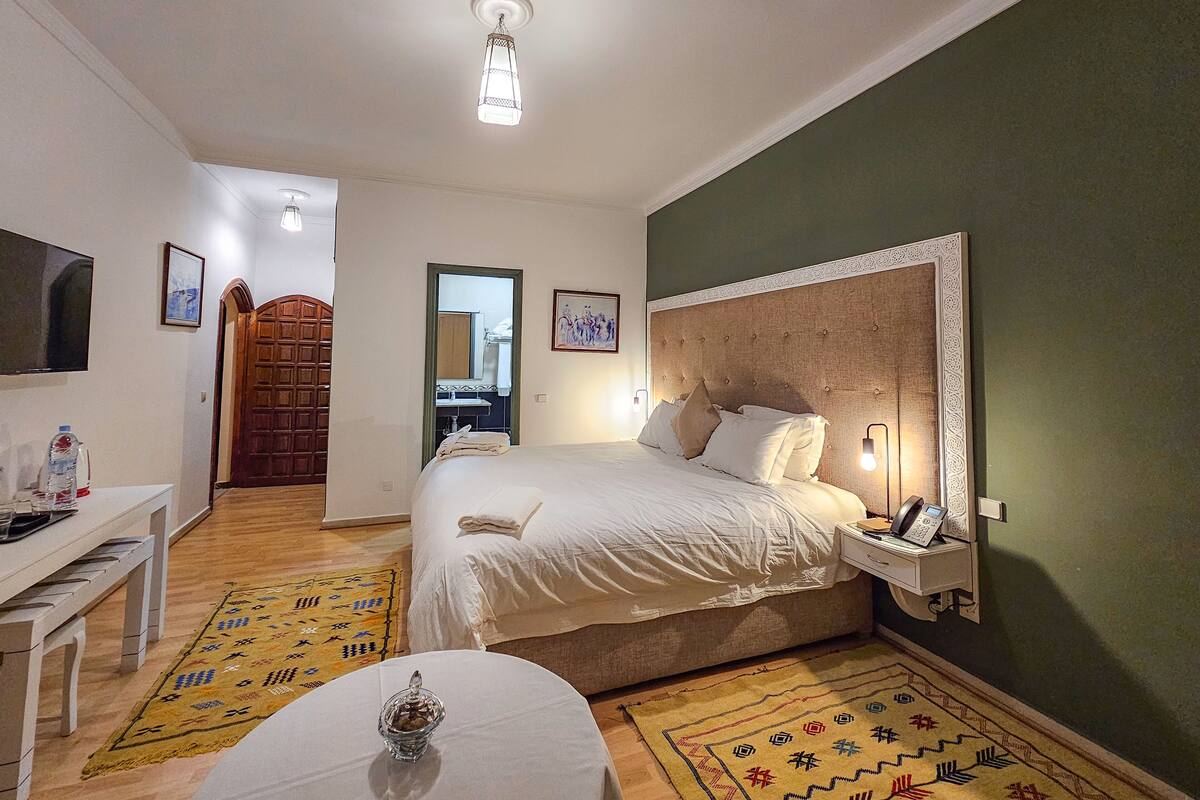 A hotel room with a bed, bedside table, lamp, and a small table with a decorative item.