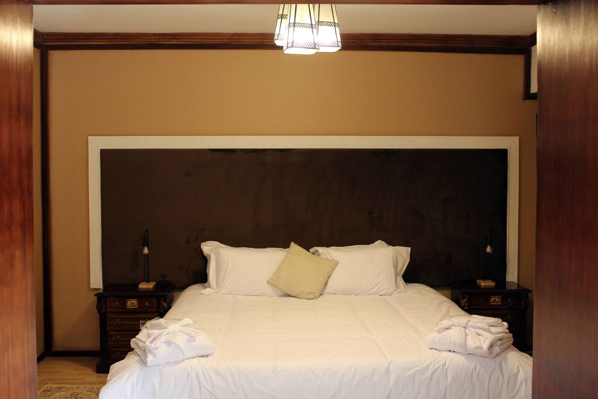 A hotel room with a large bed, wooden headboard, two bedside tables, and a chandelier.