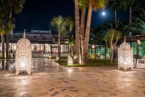 Un patio con faroles decorativos, palmeras y un edificio con balcones al fondo.