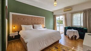 Une chambre d’hôtel avec un grand lit, une petite table, un canapé et un balcon avec des rideaux.