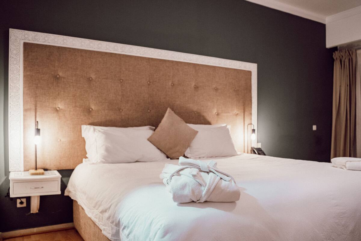 A neatly made bed with white linens and a folded robe on it.