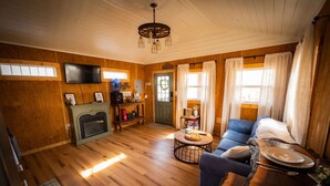 Una sala de estar acogedora con pisos de madera, chimenea, televisor y comedor con mesa y sillas.