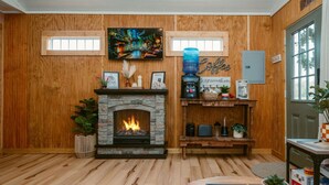 Una habitación acogedora con chimenea de piedra, paredes de madera, una zona de café y un televisor sobre la chimenea.