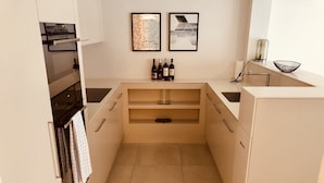 Una cocina moderna con armarios blancos, horno empotrado y una estantería para vinos con botellas.