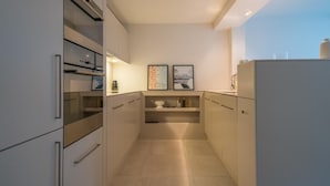 Una cocina moderna con armarios blancos, horno empotrado y dos cuadros en la pared.