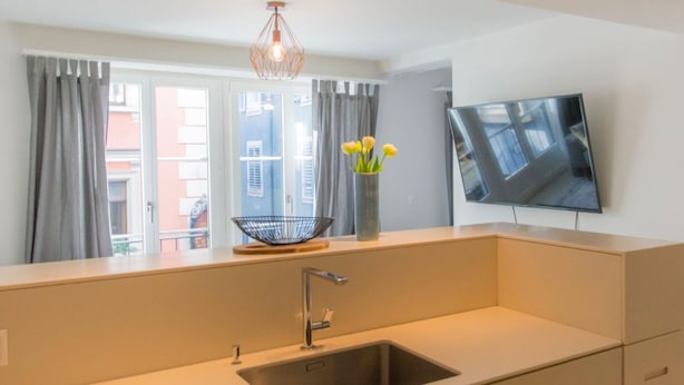 Una cocina moderna con un lavamanos empotrado, un colgante de luz y un televisor de pantalla plana montado en la pared.