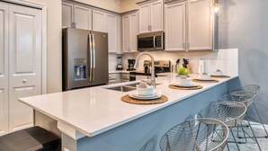 Una cocina moderna con armarios blancos, electrodomésticos de acero inoxidable y una isla central con asientos.