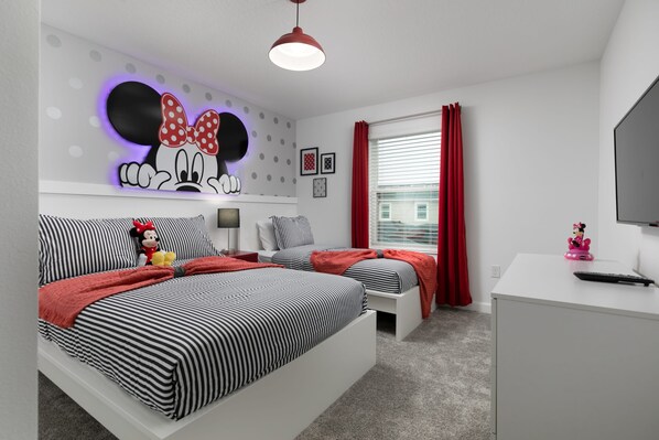 Een slaapkamer met twee bedden, een bureau en een tv aan de muur.
